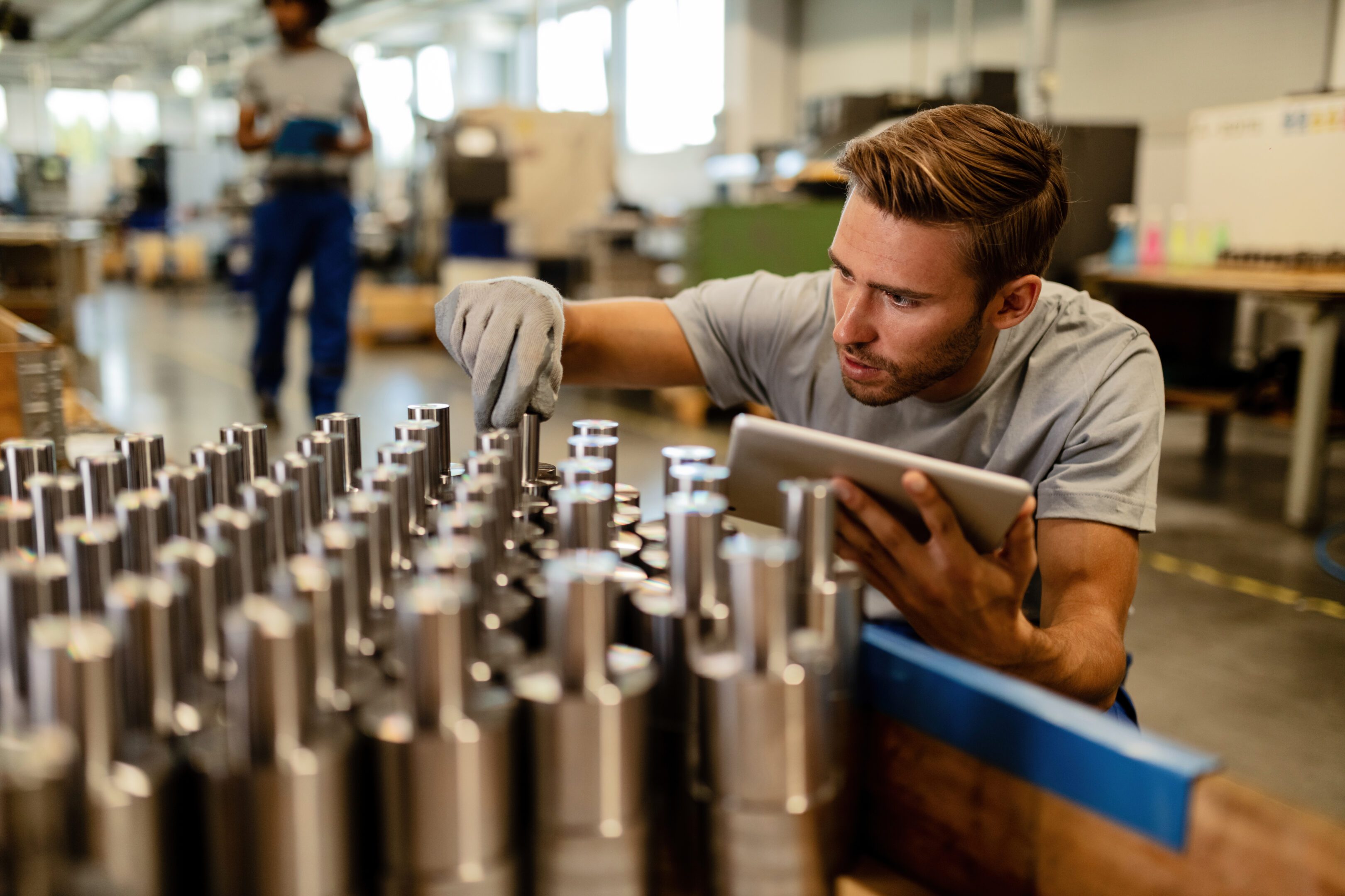 Factory worker inspecting metal components with tablet.