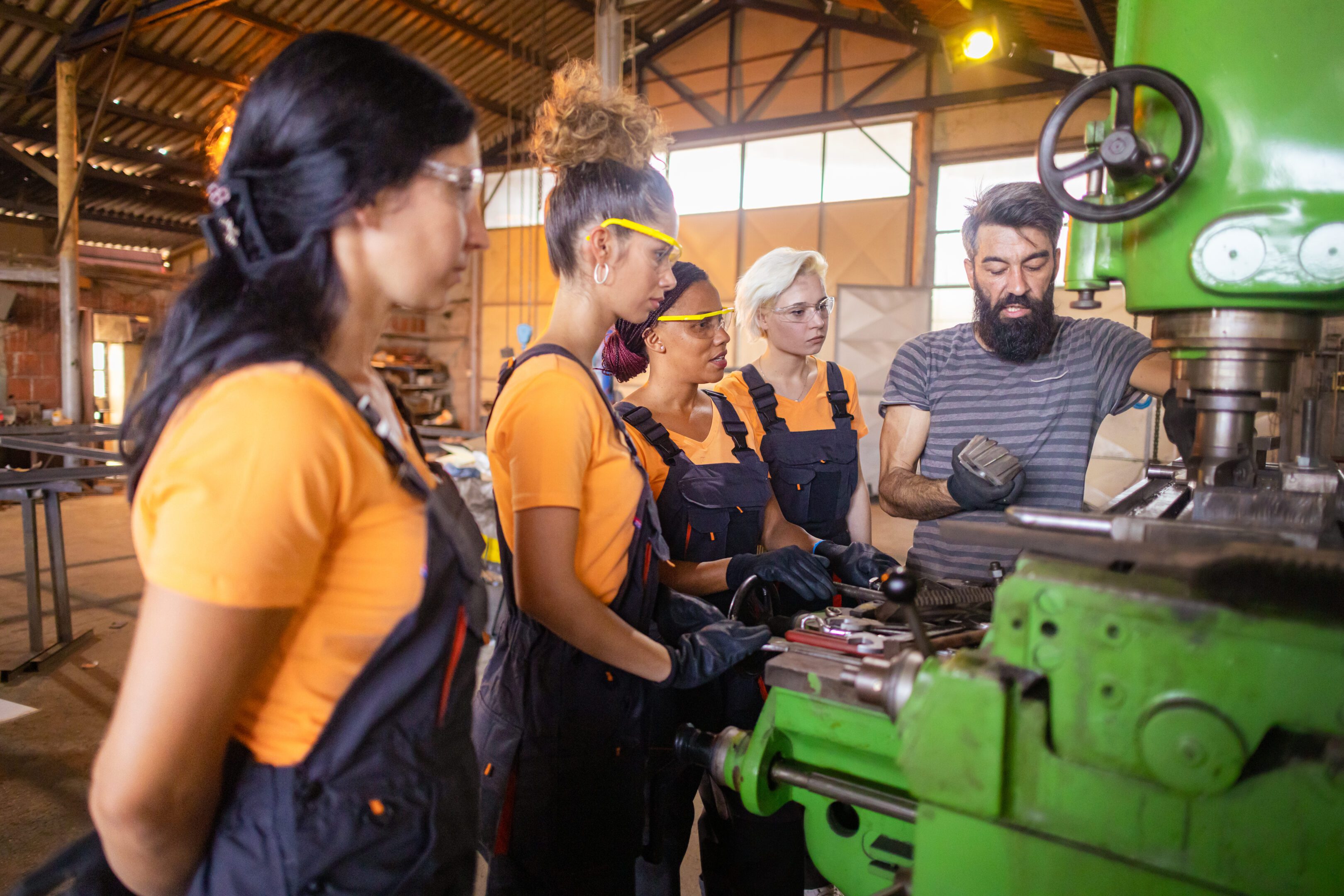 Workers learning machine operation in workshop.